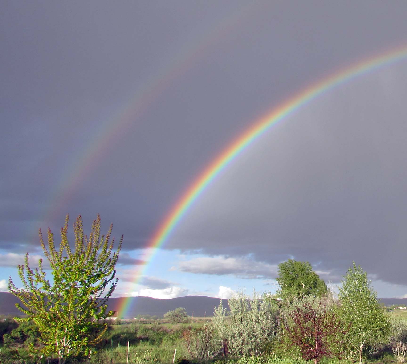 a double rainbow in a dark sky over a field in colorado
